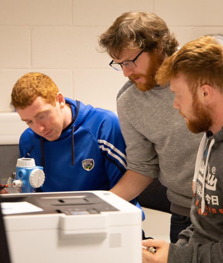 An instructor and two learners working on a machine in a classroom