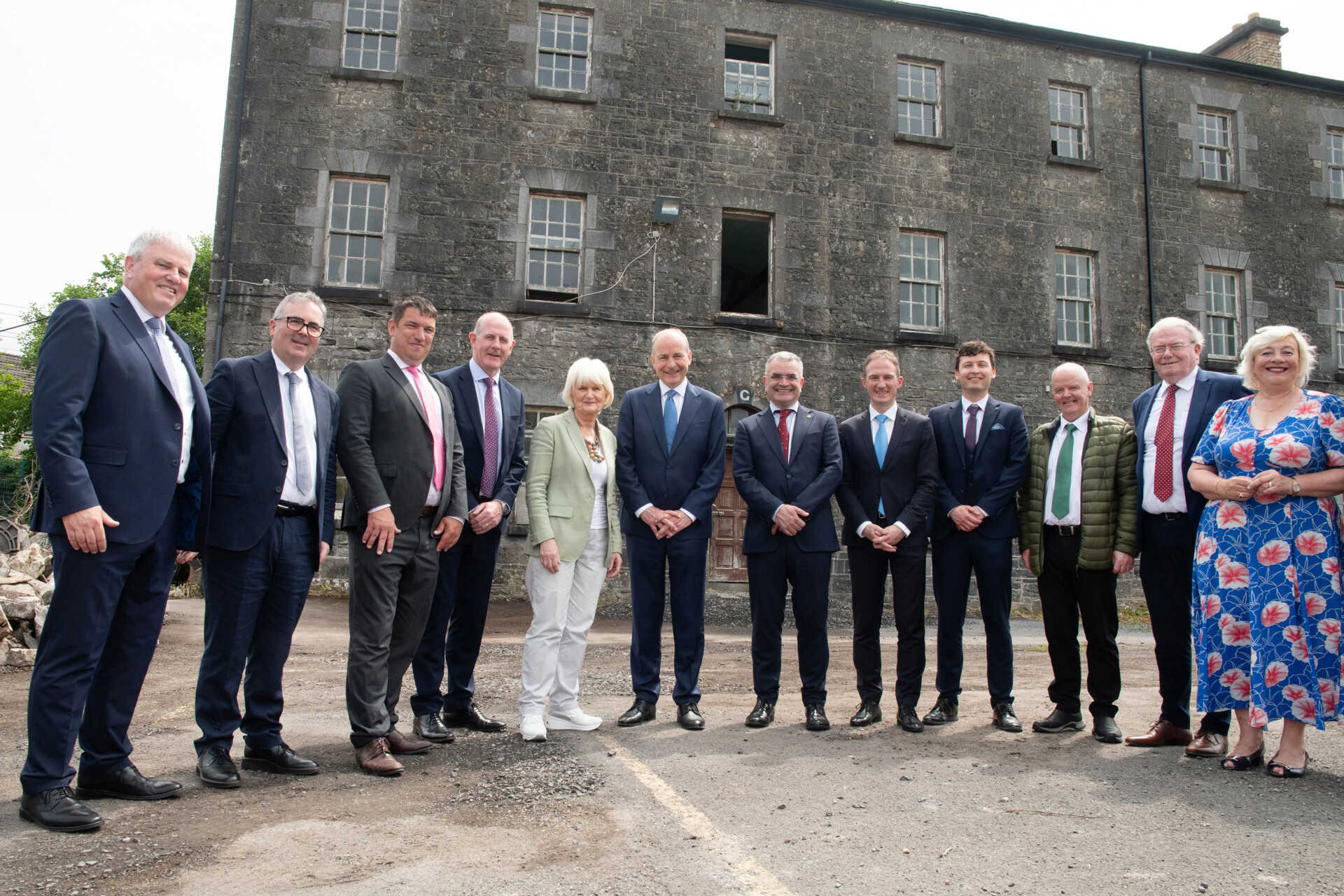 Nine men and two women standing on front of derelict stone building.