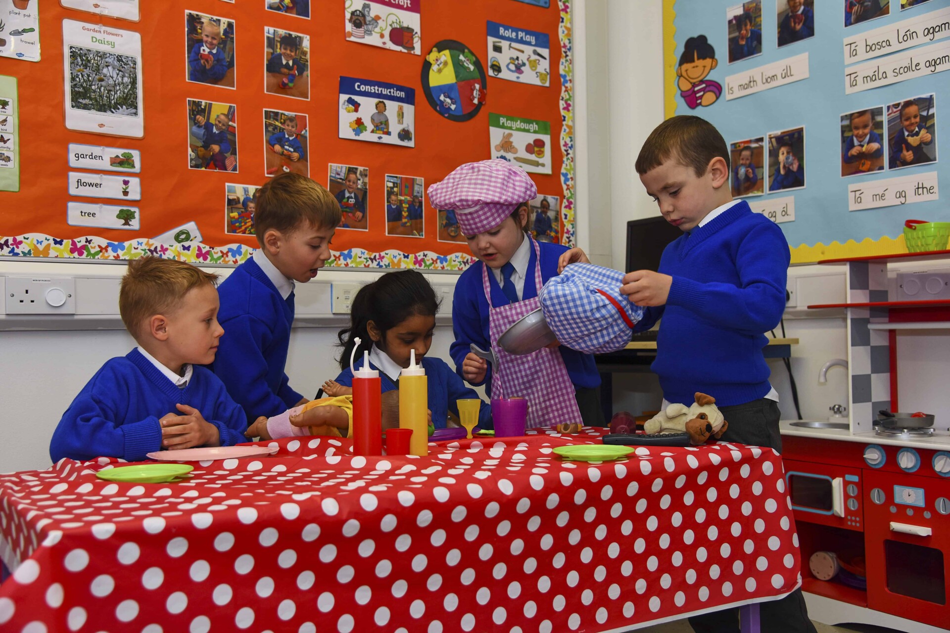 Five young students playing with food items in classroom.
