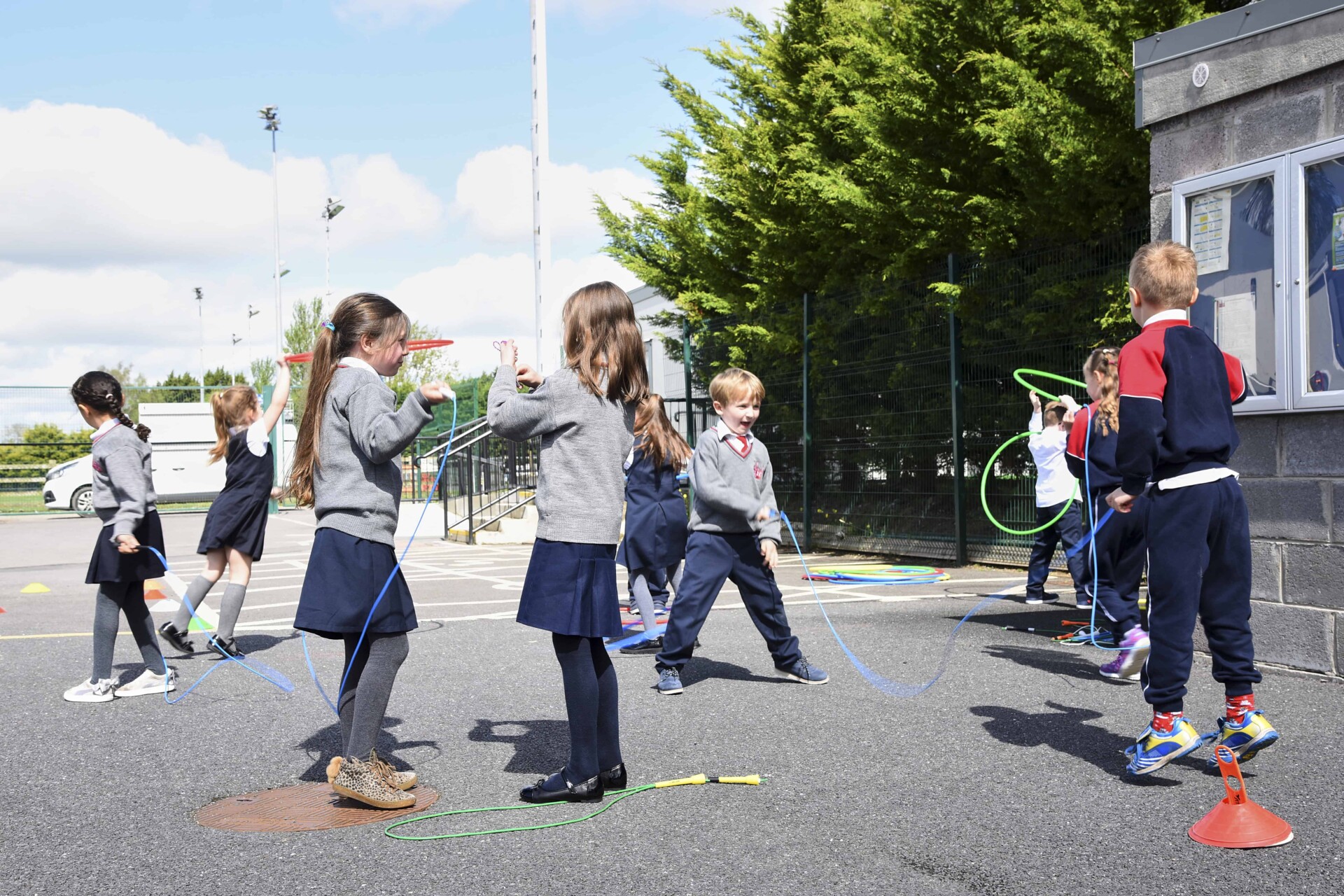 Children playing in school playground with skipping ropes and hula hoops.